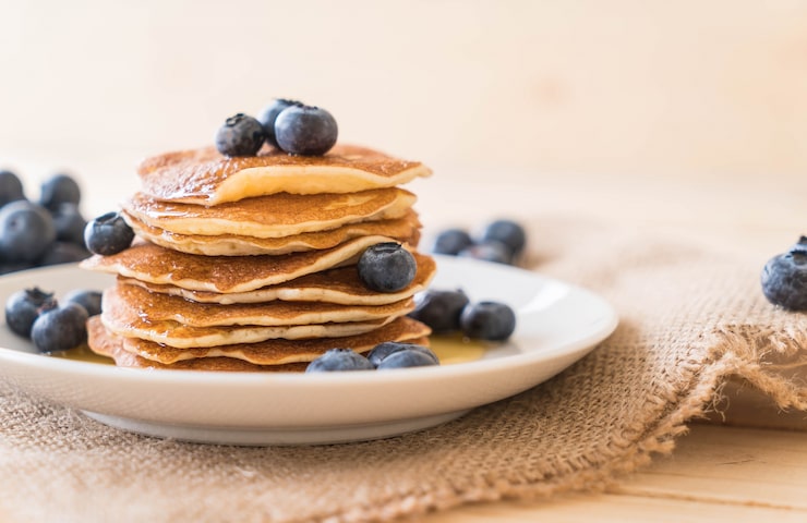 Golden protein pancakes stacked high with yogurt dollops, fresh berries, and nuts—fluffy 30g protein breakfast fuel.